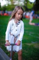 schönes Kleinkindmädchen auf dem Roller in einem Park foto