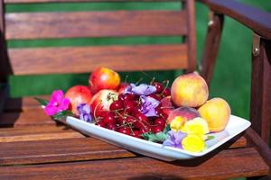 Teller mit frischen Früchten und Blumen auf Holzstühlen foto