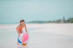 Kleines entzückendes Mädchen, das am Strand mit Ball spielt foto