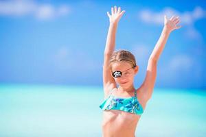 schönes kleines Mädchen am Strand, das Spaß hat. glückliches mädchen genießen sommerferien hintergrund der blaue himmel und das türkisfarbene wasser im meer auf der karibischen insel foto