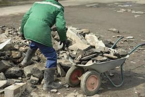 Arbeiter sammelt Steine im Wagen. Bauschutt im Gartenwagen. foto