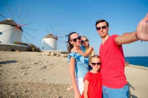 familie, die selfie mit einem stock vor windmühlen im beliebten touristengebiet auf der insel mykonos, griechenland, macht foto