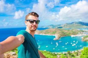 junger mann, der selfie mit blick auf den englischen hafen von shirley heights, antigua, paradiesbucht auf tropischer insel in der karibik macht foto