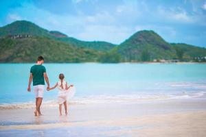 Glücklicher Vater und seine entzückende kleine Tochter am tropischen Strand, die zusammen spazieren gehen foto