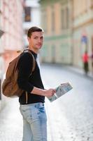 mann tourist mit stadtplan und rucksack in der europastraße. Kaukasischer Junge, der auf der Suche nach Sehenswürdigkeiten mit einer Karte der europäischen Stadt sucht. foto