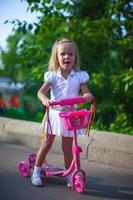 Fröhliches süßes kleines Mädchen auf dem Roller in einem Park foto