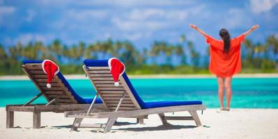 Strandliegen mit roten Weihnachtsmützen und junge Frau im tropischen Urlaub foto