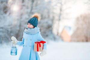 kleines mädchen, das weihnachtslaterne hält und am neuen jahr draußen am schönen winterschneetag präsentiert foto