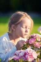 Kleines entzückendes Mädchen, das draußen bunte Blumen riecht foto