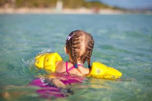 Entzückendes kleines Mädchen, das im tropischen Strandurlaub im Meer schwimmt foto
