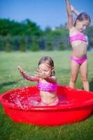 Zwei kleine Schwestern, die in ihrem Garten in einem kleinen Pool herumtollen und planschen foto