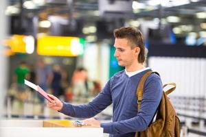 junger Mann mit Pässen und Bordkarten an der Rezeption am Flughafen foto