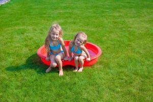 Zwei kleine Schwestern, die in ihrem Garten in einem kleinen Pool herumtollen und planschen foto
