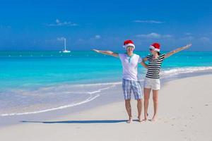 junges glückliches Paar in roten Weihnachtsmützen am tropischen Strand foto