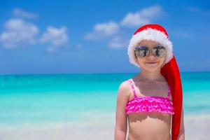 kleines süßes mädchen im roten hut weihnachtsmann am strand foto