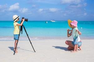 Kleines Mädchen, das am Strand ein Foto von ihrer Mutter und ihrer Schwester macht