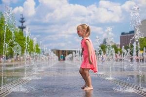 Kleines glückliches Mädchen hat Spaß im Straßenbrunnen an heißen sonnigen Tagen foto