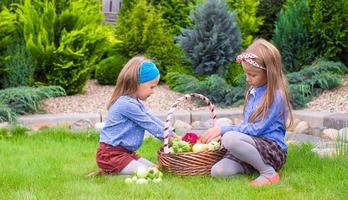 Zwei kleine glückliche Mädchen mit großer Herbsternte von Tomaten in Körben foto