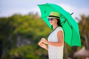 junges Mädchen mit grünem Regenschirm am weißen Strand foto