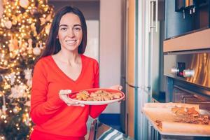 junge frau in weihnachtsmütze, die zu hause lebkuchen backt. foto