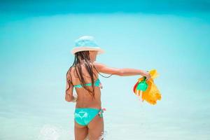 Entzückendes kleines Mädchen, das mit Strandspielzeug am weißen tropischen Strand spielt foto