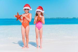 Entzückende kleine Mädchen mit Seesternen am weißen leeren Strand foto