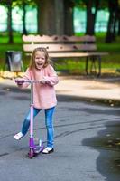 entzückendes kleines Mädchen hat Spaß auf dem Roller im Freien foto