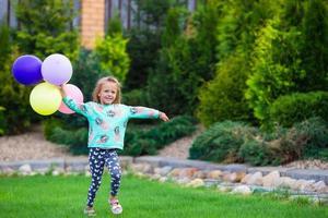 glückliches kleines Mädchen, das draußen mit Luftballons spielt foto