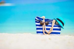 Strandzubehör - blaue Tasche, Strohhut, Sonnenbrille am weißen Strand foto