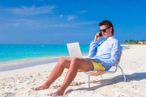 junger Mann, der am Laptop am tropischen Strand arbeitet foto