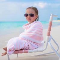 entzückendes kleines Mädchen mit Sonnenbrille, bedeckt mit Handtuch am tropischen Strand foto