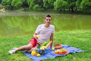 junger glücklicher Mann, der im Park picknickt und sich entspannt foto