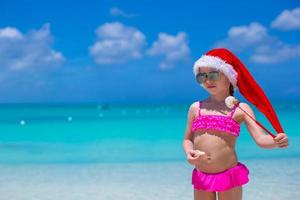 kleines entzückendes mädchen in roter weihnachtsmütze genießen strandurlaub foto