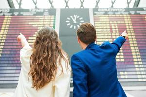 junger Mann und Frau im internationalen Flughafen mit Blick auf die Fluginformationstafel foto