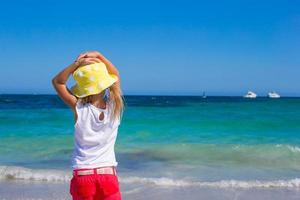 entzückendes kleines Mädchen, das im seichten Wasser am weißen Strand spielt foto