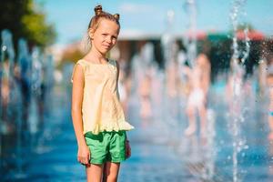 Kleines entzückendes Mädchen hat Spaß im Straßenbrunnen an heißen sonnigen Tagen foto