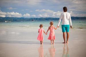 Rückansicht des Vaters und seiner beiden kleinen Töchter, die am Meer spazieren gehen foto