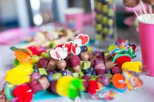 Canape aus Obst, weiße Schokoladenkuchen und Popcorn auf dem süßen Kindertisch bei der Geburtstagsfeier foto