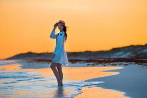 junge schöne Frau an der tropischen Küste im Sonnenuntergang. glückliches Mädchen im Kleid am Abend am Strand foto