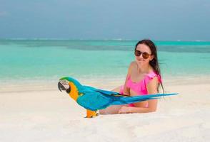 entzückendes Mädchen am Strand mit buntem Papagei foto