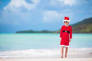 entzückendes kleines Mädchen in der Weihnachtsmütze am tropischen Strand foto