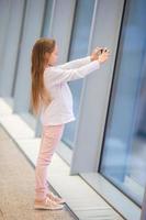 kleines Mädchen im Flughafen in der Nähe des großen Fensters, während es auf das Boarding wartet foto