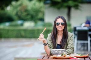 junge Frau, die auf der Straße Nudeln zum Mitnehmen isst foto