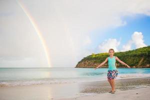 glückliches kleines Mädchen im Hintergrund der schöne Regenbogen über dem Meer. schöner Regenbogen am karibischen Strand foto