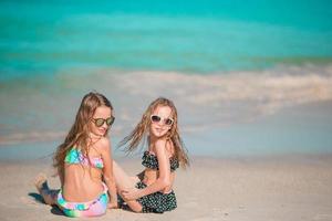 Entzückende kleine Mädchen, die mit Sand am Strand spielen. Kind sitzt im seichten Wasser foto