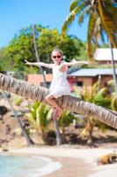 glückliches Kind, das während des Karibikurlaubs am weißen Strand auf einer Palme sitzt foto