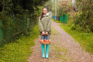 junge Frau in Gummistiefeln mit Apfelkorb in den Händen zur Herbstzeit foto