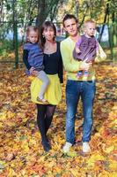 junge charmante vierköpfige Familie, die im gelben Herbstpark spazieren geht