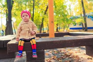 kleines schönes Mädchen sitzt auf einer Bank im Herbstpark foto