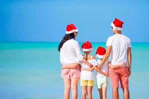 glückliche familie in roten weihnachtsmützen an einem tropischen strand, der weihnachtsferien feiert foto